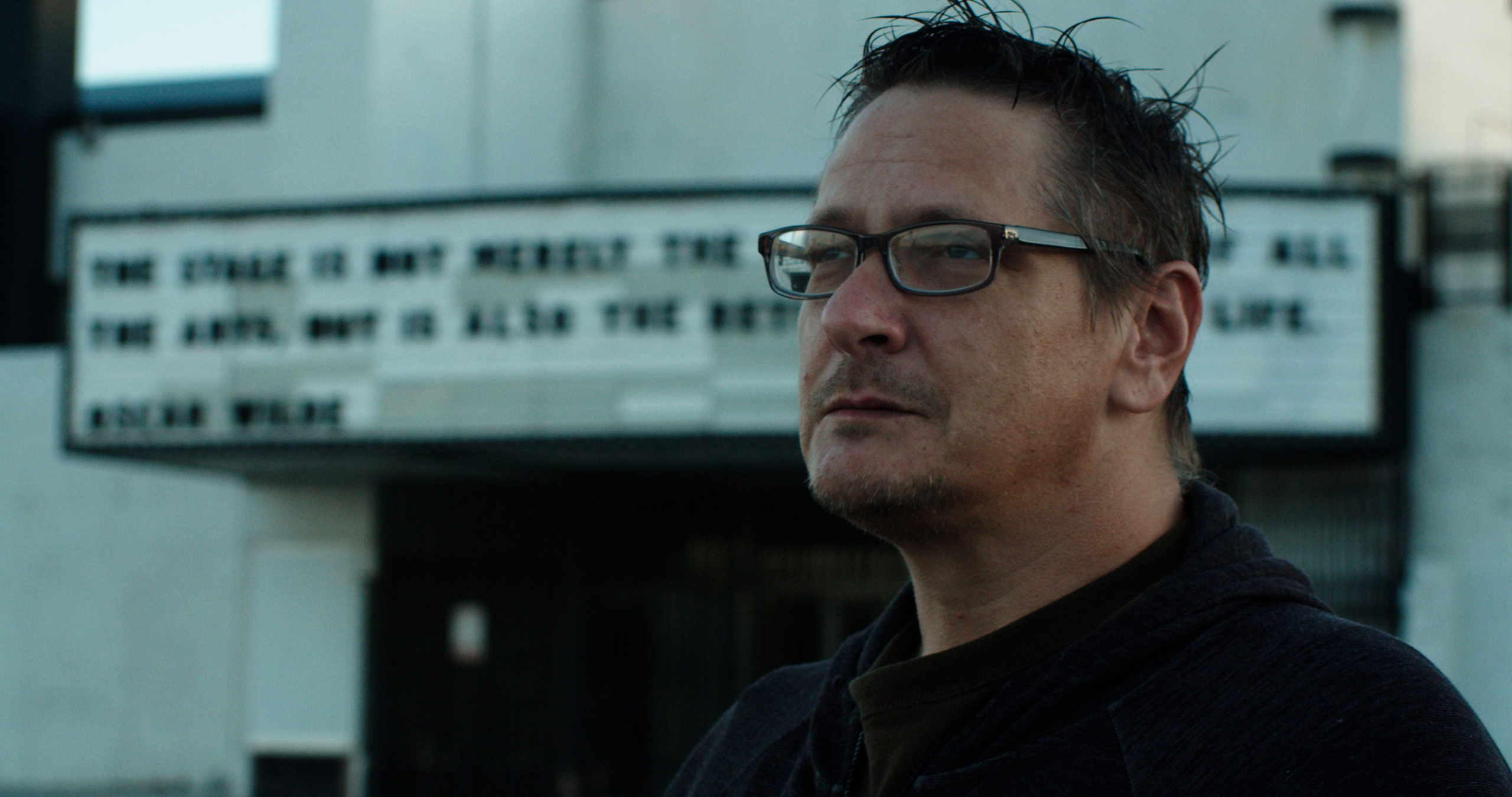 Man in glasses standing in front of a theater marquee