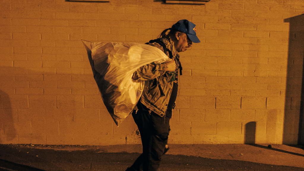 Homeless man carrying a trash bag through an alley